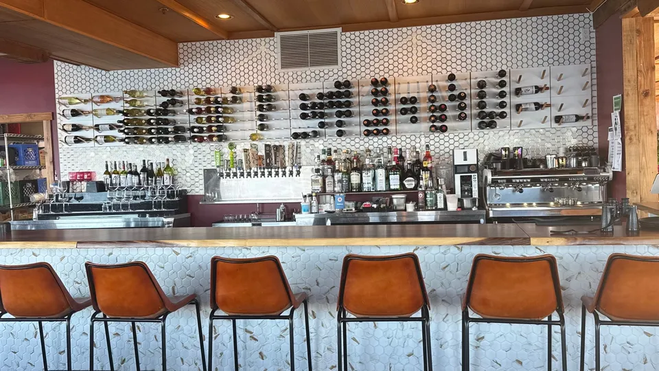 The bar in daylight: eight leather stools along a white tiled counter, with wine racked on the wall behind