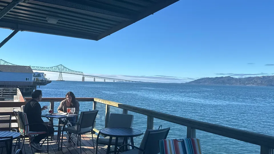 The covered deck on a clear day, tables along the railing with the river and the bridge beyond