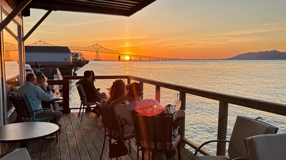 Guests on the covered deck at sunset, the bridge and the river beyond the railing