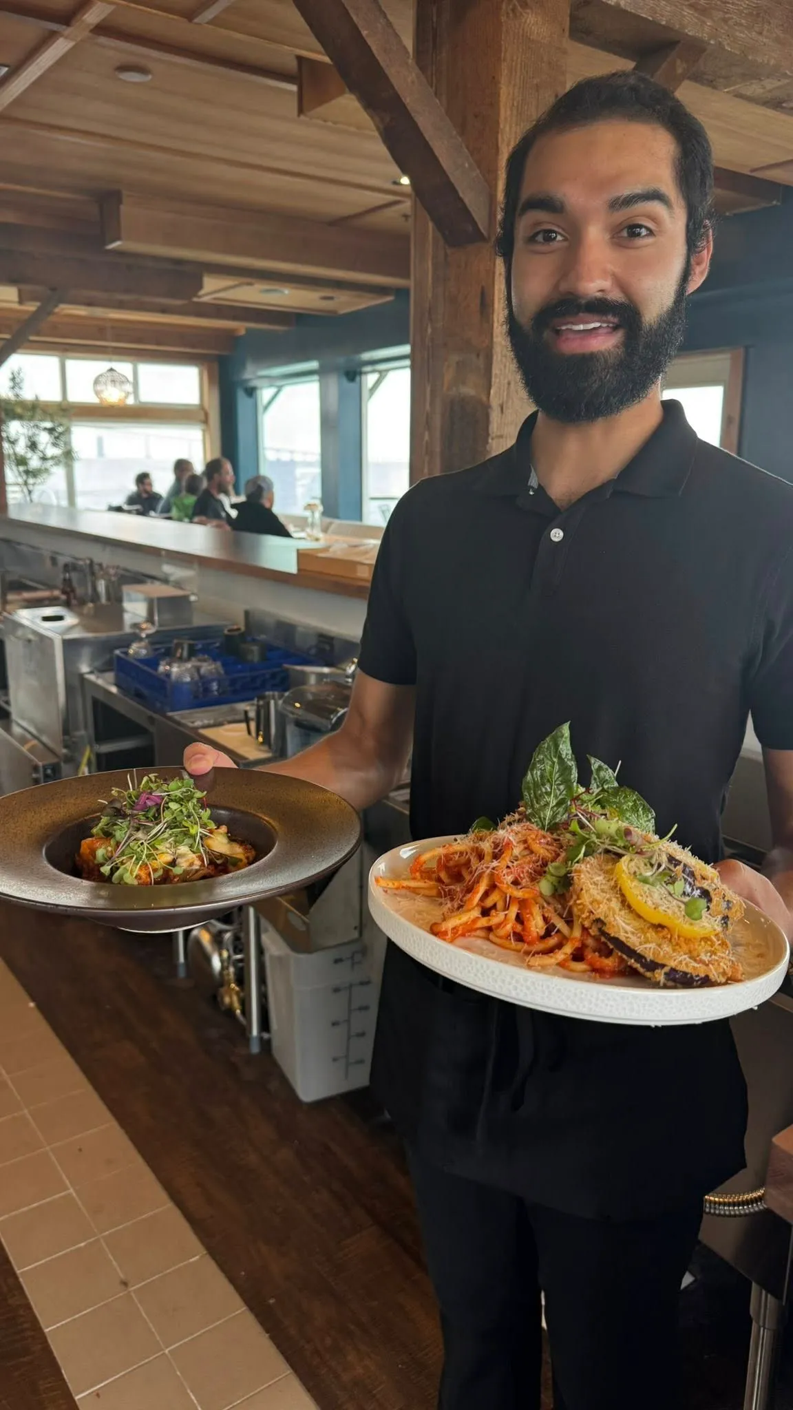 A server carrying two plates out of the kitchen, pasta in one hand and a salad in the other