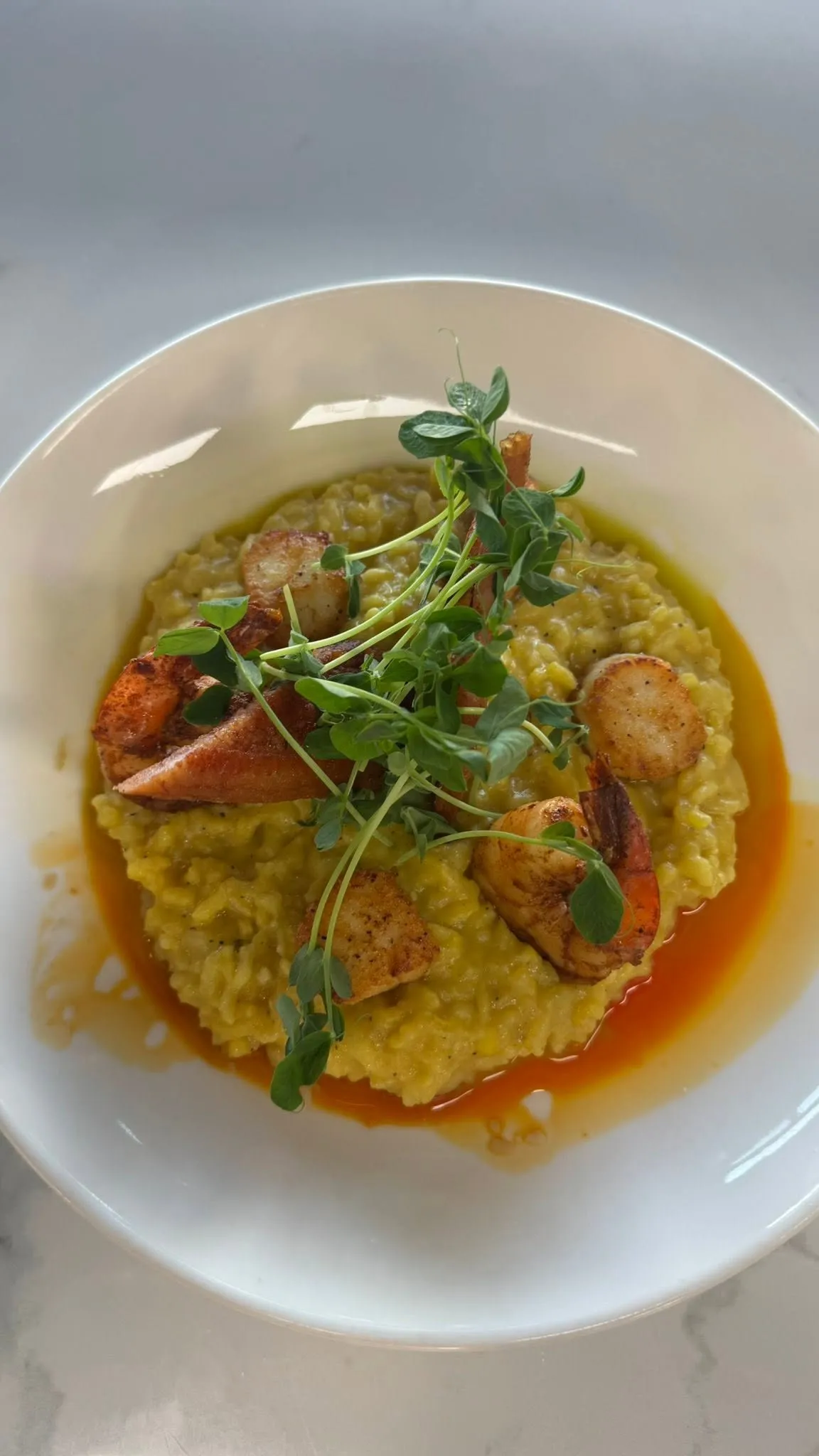 Seafood risotto with seared scallops and shrimp, topped with pea shoots, in a white bowl